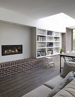 Spacious living room with a minimalist design, featuring a long horizontal fireplace, built-in white bookshelves, and a continuous brick bench. Booterstown, Dublin
