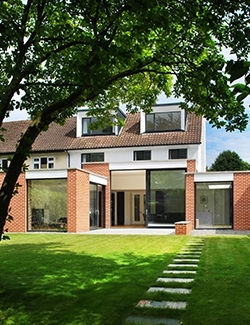 Front view of a modern home renovation project in North Dublin featuring large windows and a unique roof design, with a beautifully landscaped garden