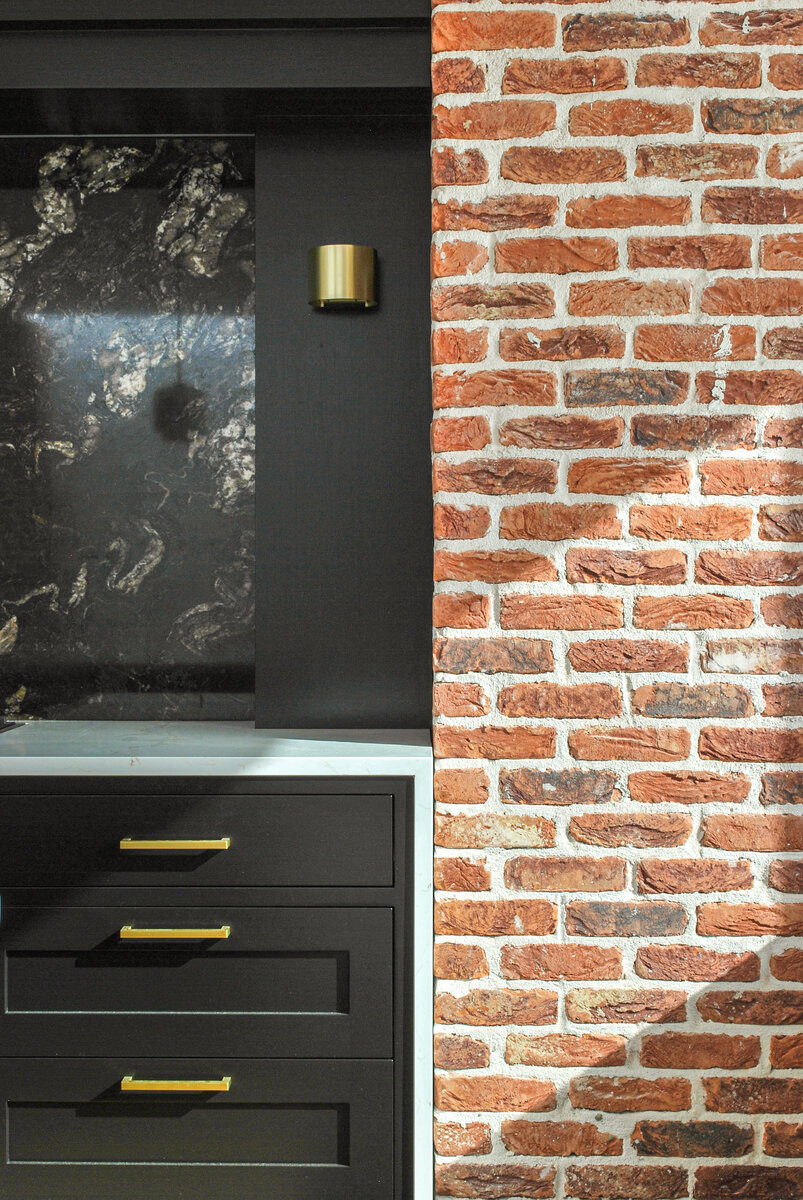 A detail of various materials used in the kitchen including brickwork, black cabinetry, white stone counter tops and brass details