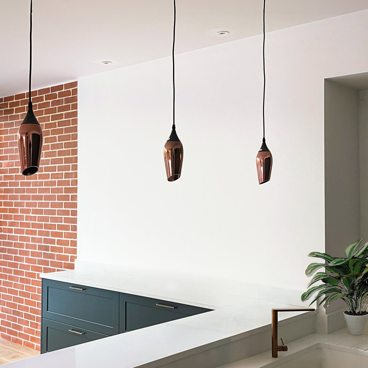 The kitchen area is simple and modern with dark green timber cabinetry and brass light fittings