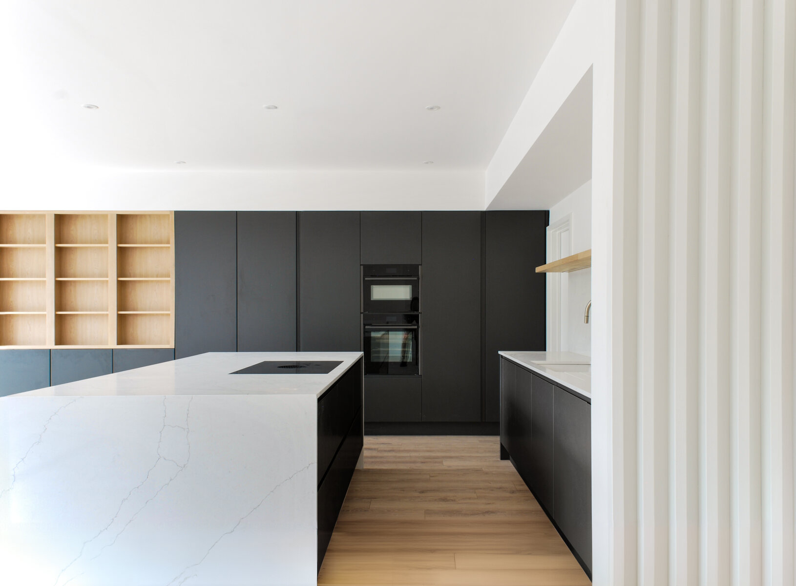 Dark kitchen cabinets with white marble counter and oak shelving